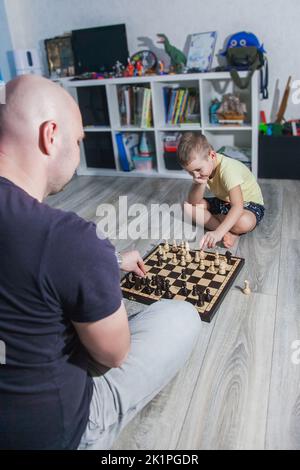 Dad and son play chess on the floor in the children's room among the toys. Stock Photo
