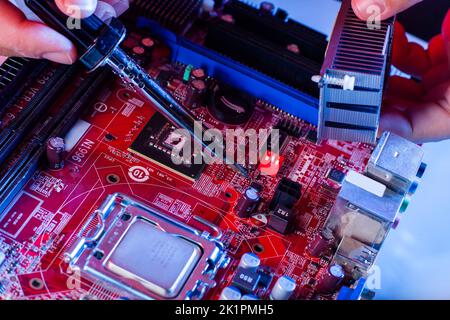 A man soldering a motherboard. Repair and maintenance of desktop personal computers and laptops. Stock Photo