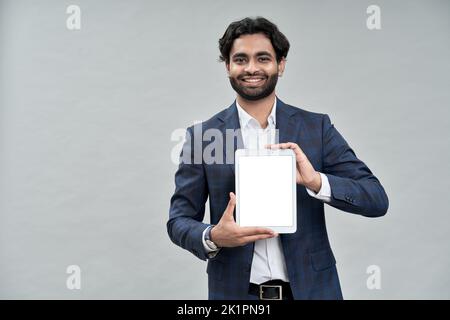 Smiling indian business manager wearing suit showing digital tablet mockup. Stock Photo