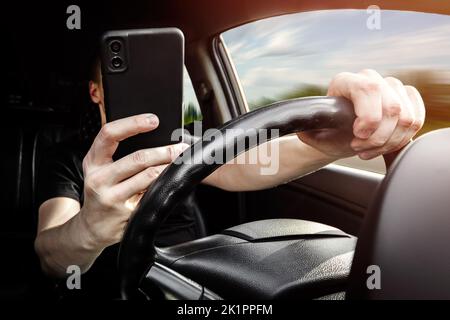 The driver at the wheel of a car uses a smartphone, distracted from the road Stock Photo