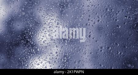 Water drops on wet window, raindrops on blue window glass. Selective focus, bokeh. Blurred rainy city background. Autumn abstract backdrop. Rain drops Stock Photo