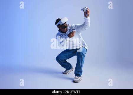 Gamer exploring virtual reality video games in a studio. Young man gaming with virtual reality goggles and controllers. Active young man experiencing Stock Photo