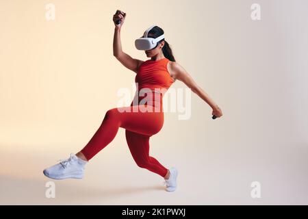 Energetic young woman working out using 3D technology. Sporty young woman exploring a virtual reality fitness game. Athletic young woman wearing virtu Stock Photo