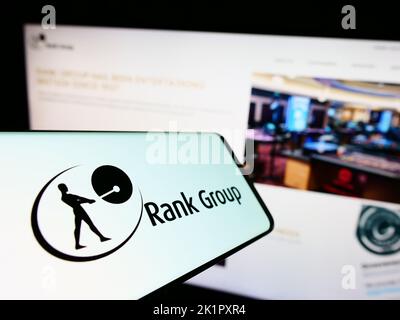 Cellphone with logo of British gambling company The Rank Group plc on screen in front of business website. Focus on center-left of phone display. Stock Photo