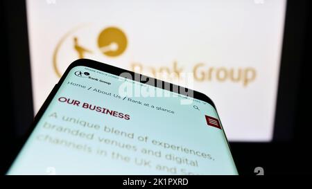 Mobile phone with website of British gambling company The Rank Group plc on screen in front of business logo. Focus on top-left of phone display. Stock Photo