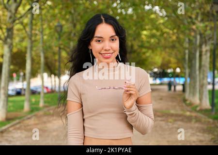Young latin girl holding her glasses and smiling looking ar camera. Stock Photo