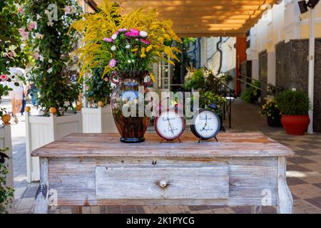Autumn still life with a retro clock, a bouquet of autumn flowers in a glass vase standing on an antiques table of a roadside cafe. Stock Photo