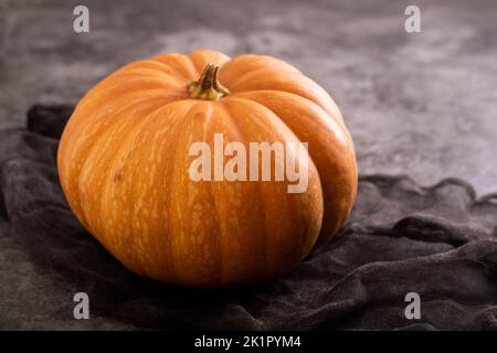 Fresh orange pumpkin with napkin on grey ceramic. Stock Photo