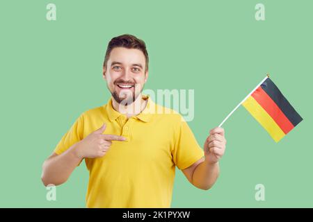 Happy young man isolated on green background holding flag of Germany and smiling Stock Photo
