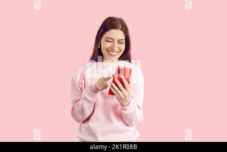 Joyful young woman on pastel pink background swipes and scrolls on screen of mobile phone. Stock Photo