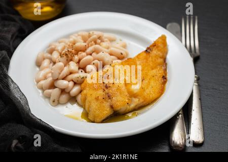Fried cod fish with white beans on the plate. Stock Photo