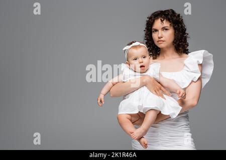 Curly woman in white dress holding baby girl isolated on grey,stock image Stock Photo