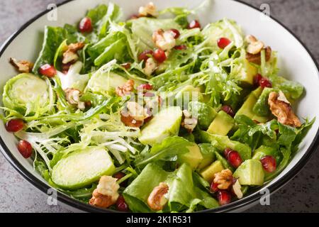 Raw Healthy salad with Brussels Sprouts Pomegranate, Avocado, walnuts and lettuce closeup in the bowl on the table. Horizontal Stock Photo