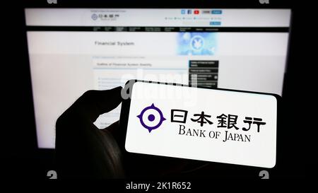 Person holding cellphone with logo of financial institution Bank of Japan (BOJ) on screen in front of web page. Focus on phone display. Stock Photo