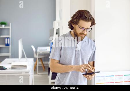 Businessman in casual T shirt standing in office, holding mobile phone and making business call Stock Photo