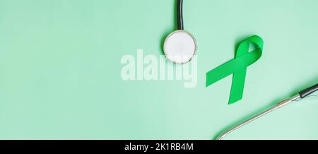 green Ribbon with stethoscope on green color background for supporting people living and illness. Liver, Gallbladders bile duct Cancer and organ donat Stock Photo