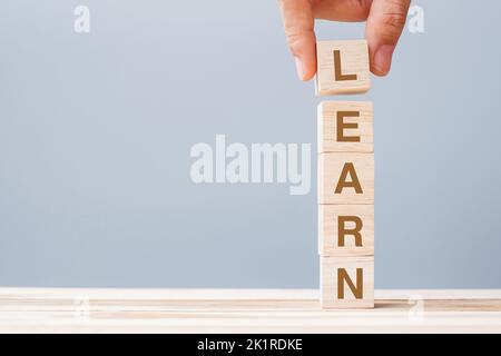 Business man hand holding wooden cube block with LEARN business word on table background. Learning, Education Knowledge, Studying and Wisdom Stock Photo