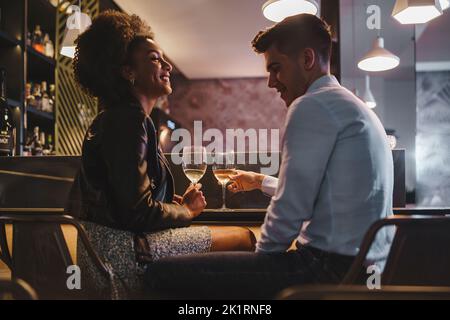 Romantic couple on a date talking holding a glass of white wine sitting at the bar counter in the night - food and drink, people, lifestyle concept Stock Photo