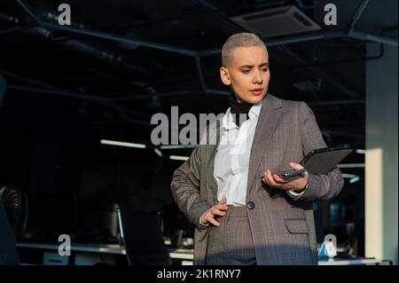 Pensive young woman with short hair uses mobile phone in office. Stock Photo