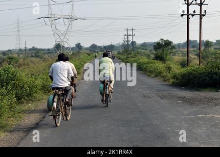 A beautiful photo of an Indian old and young man farmer riding his bicycle (bike or cycle) in a nearby village along the fields or farmlands or farms Stock Photo