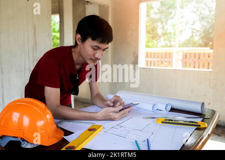 Engineer or Architect using cell phone on blueprint in building construction site. Stock Photo