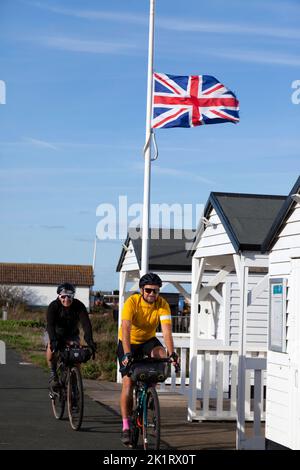 Two smiling,  male cyclists, pass under a union Jack flying at half mast,  during the period of national mourning, for Queen Elizabeth 2nd. Stock Photo