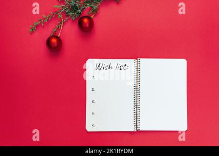 Wish list. Open blank spiral notebook for writing list of dreams and goals. Christmas tree branch with decorations on trendy red background. Copy space text, to-do list. Planning 2023. Minimal style. Stock Photo