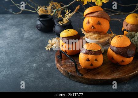 Halloween party jack-o-lantern chocolate orange cakes against the background of the old forest, branches and leaves. Halloween food concept. Sweets fo Stock Photo