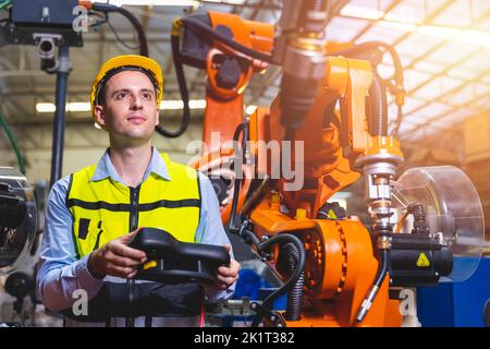 Caucasian engineer male worker working in metal factory with robot welding machine programmer controller and monitor. Stock Photo