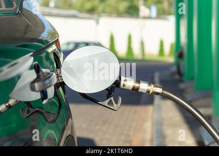 Fuel nozzle to refill fuel in car at gas station. Red fuel dispenser on gray car in petro station. Stock Photo