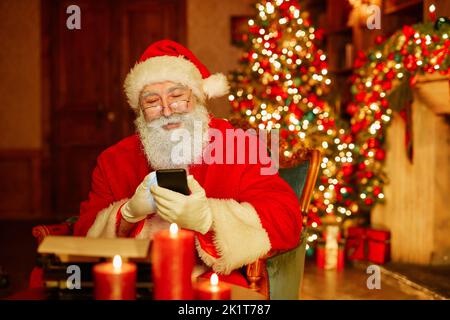 Portrait of traditional Santa Claus using smartphone in festive room with Christmas decorations, copy space Stock Photo