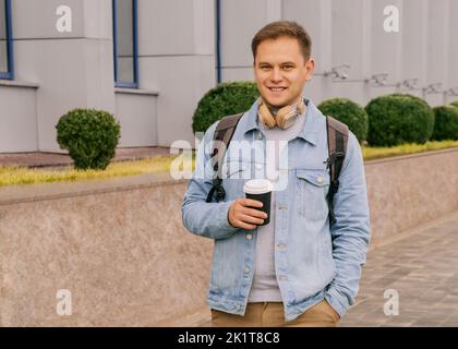 Young man in headphones with backpack is drinking coffee Stock Photo
