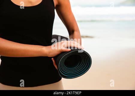 Woman in sport suite carry yoga mattress on the beach,Sport background.healthy lifestyle and travel. Sport female equipment Stock Photo