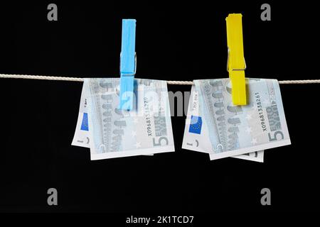 Five euro banknotes fastened with clothespins are dried on a clothesline on dark background Stock Photo