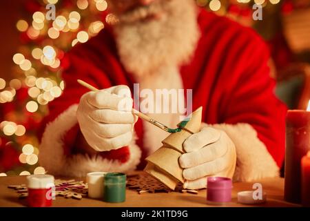 Close up of traditional Santa Claus painting wooden toys in workshop on Christmas eve, copy space Stock Photo
