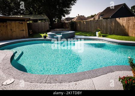 A large free form gray grey accent swimming pool with turquoise blue water in a fenced in backyard in a suburb neighborhood Stock Photo