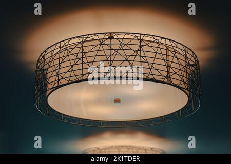 A glowing and lit drum light with black metal accents on a warm ceiling Stock Photo