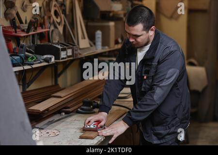 Waist up portrait of Caucasian male worker sanding wood plank in workshop Stock Photo