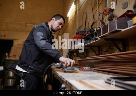 Side view portrait of male worker sanding wooden boards in workshop and using electric tools, copy space Stock Photo
