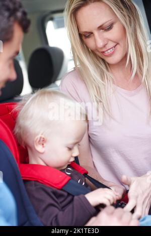 Making sure our son is safe. A mother and father helping their child in a baby seat for the car. Stock Photo