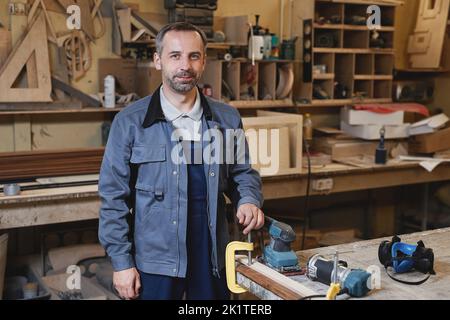 Waist up portrait of smiling male worker looking at camera while standing in factory workshop, copy space Stock Photo