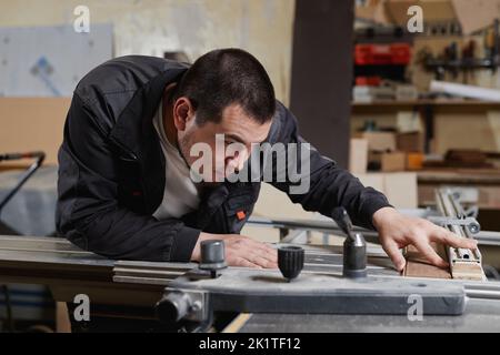 Side view portrait of male worker using wood cutting machine in workshop and measuring carefully Stock Photo