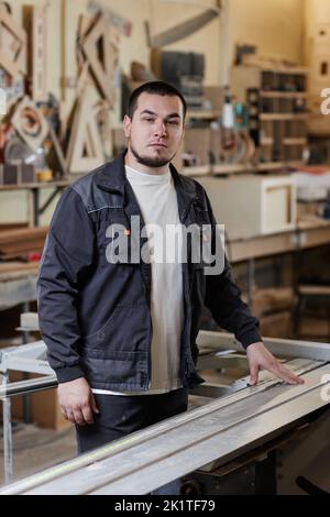 Vertical portrait of male worker standing in workshop at woodworking factory and looking at camera Stock Photo
