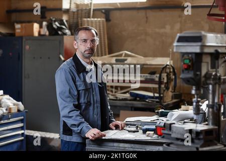 Waist up portrait of mature worker looking at camera while standing in factory workshop, copy space Stock Photo