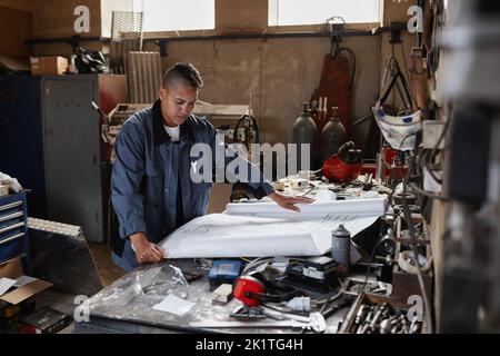 Portrait of modern female worker looking at plans and blueprints in factory workshop, copy space Stock Photo