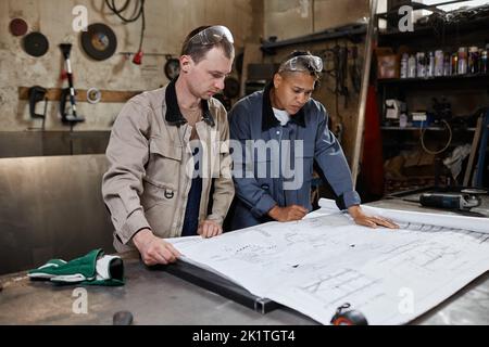 Portrait of two workers looking at blueprints and plans in industrial factory workshop Stock Photo