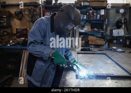 Side view portrait of female welder working with metal in industrial workshop, copy space Stock Photo