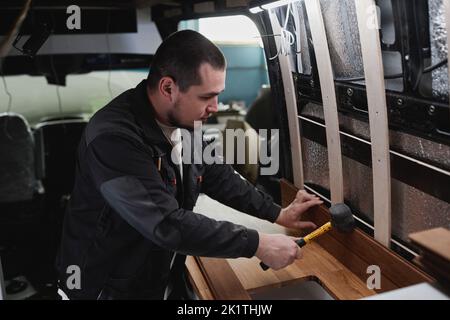 Side view portrait of young man building camper van and installing furniture in kitchen area Stock Photo