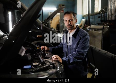 Waist up portrait of mature car mechanic repairing trucks in garage and looking at camera with accent light, copy space Stock Photo
