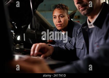 Portrait of female mechanic using laptop during car checkup in garage with accent light Stock Photo